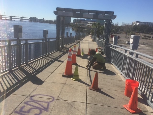 A muralist kneeled on sidewalk with cones blocking area to be painted