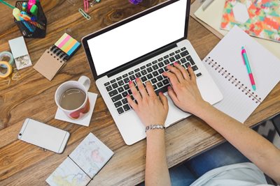 woman working on a laptop at a desk filled with brightly colored office supplies