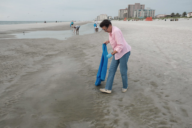 older woman in pink shirt picking up trash on the beach